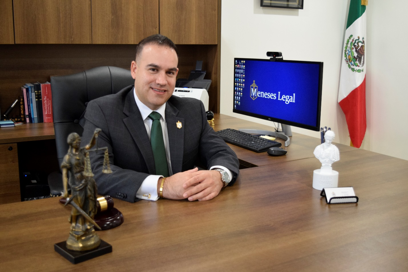 A lawyer sitting at a desk next to a computer and the Mexican flag