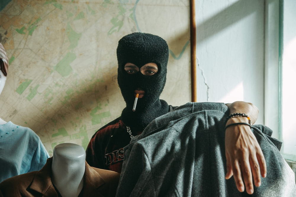 A gang member wearing a balaclava sitting in front of a map smoking a cigarette