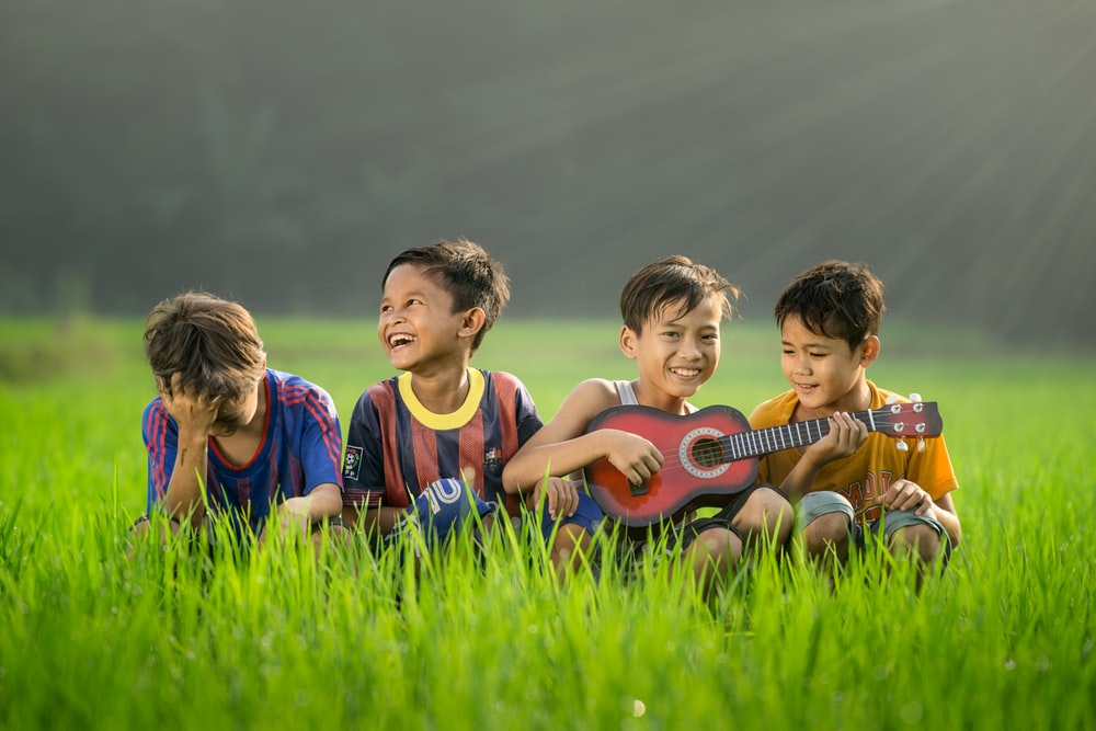 A boy playing guitar next to three other boys in a meadow