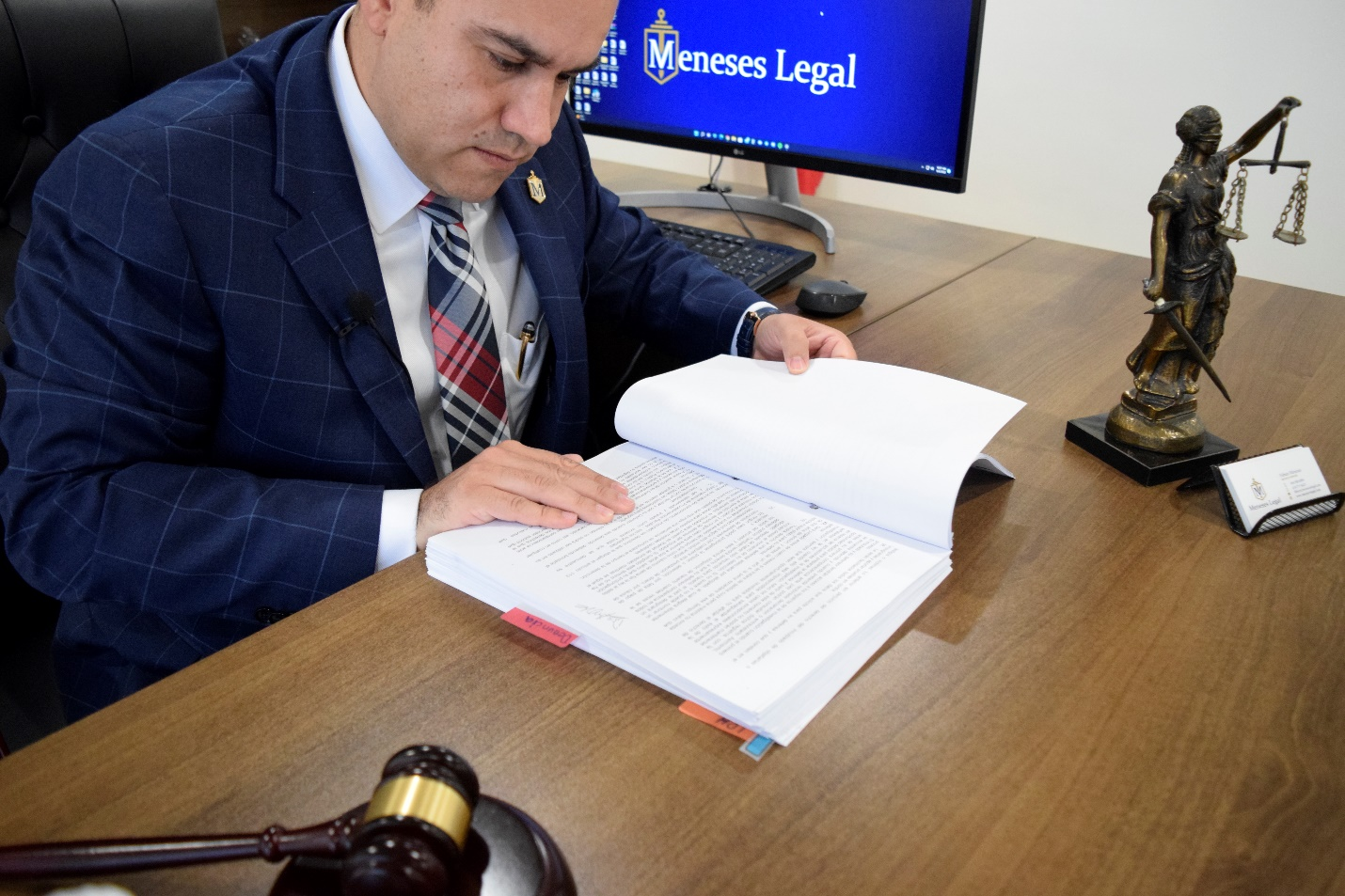 A lawyer sat at a desk reading a document next to a gavel and a computer