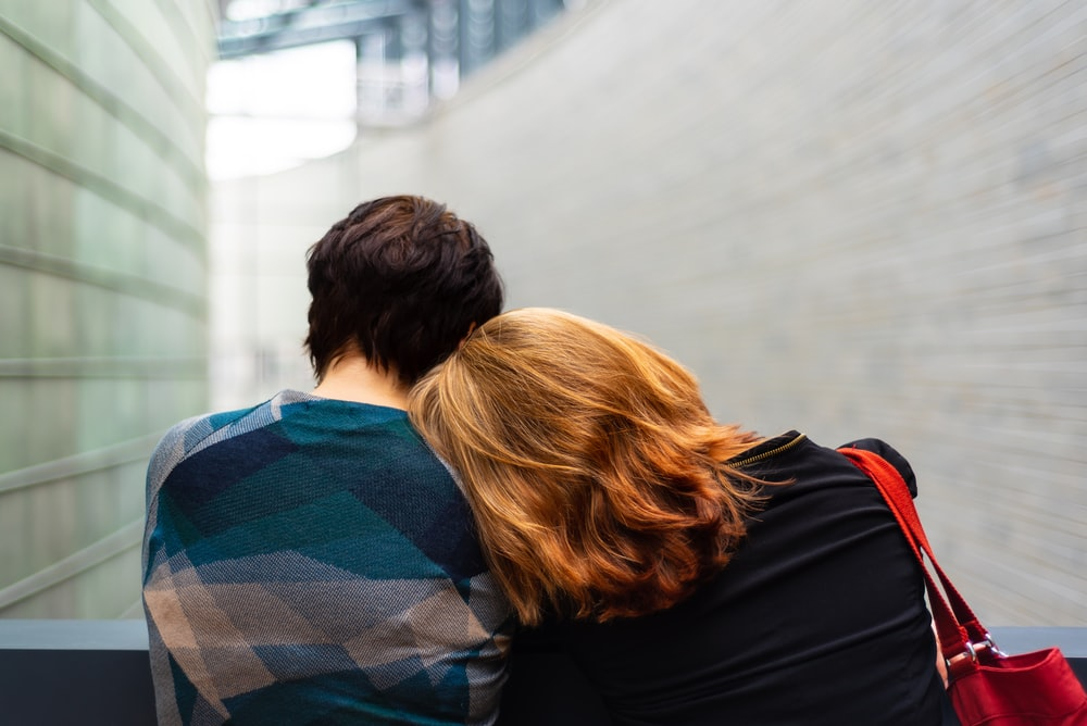 A woman with a handbag leaning against another person in front of a wall