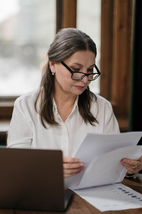 A woman sitting in front of a laptop looking through documents